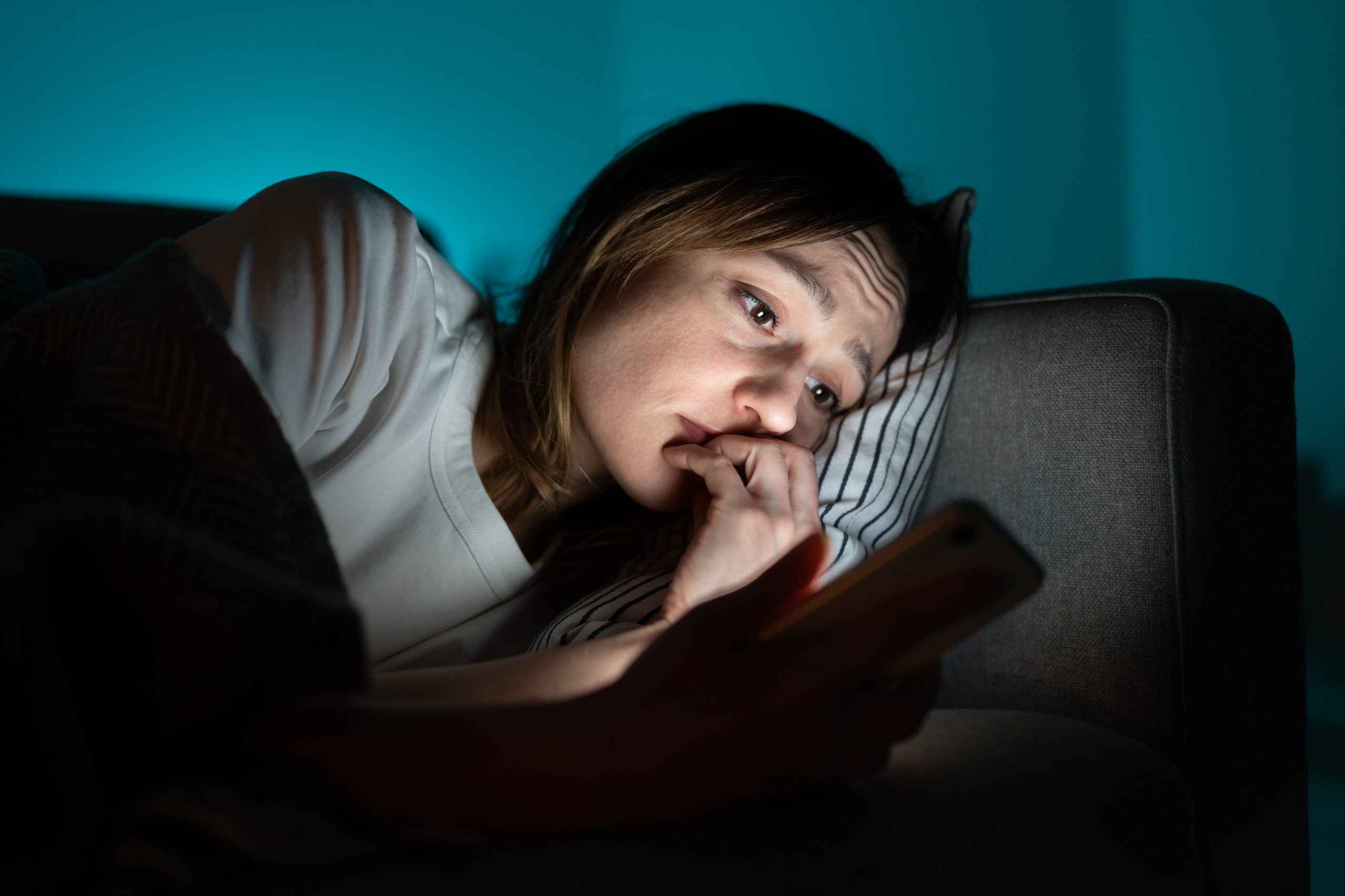 Person lying in bed at night, looking at their phone screen in the dark